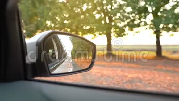 汽车在日落时穿过被树木包围的道路时从后视镜中观看视频的预览图