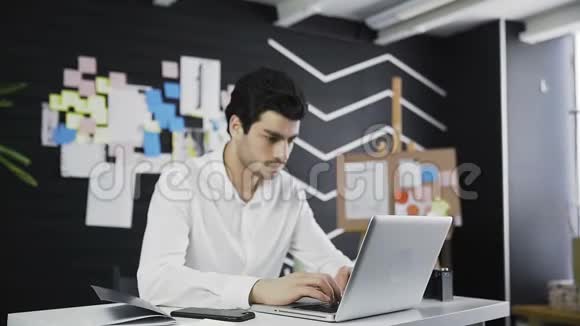 一个英俊的男人办公室经理看着坐在他工作场所的相机视频的预览图