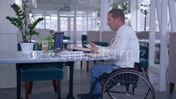 在网上教育期间坐在桌子上的残疾人坐在轮椅上用笔记本电脑上的应用程序说话视频的预览图
