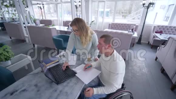 对残疾的坐轮椅的老年男子进行专业培训在个别情况下由妇女使用手提电脑视频的预览图