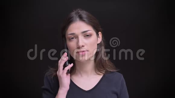 年轻的白种人长发黑发女孩在黑色背景下的智能手机上专心交谈的肖像视频的预览图