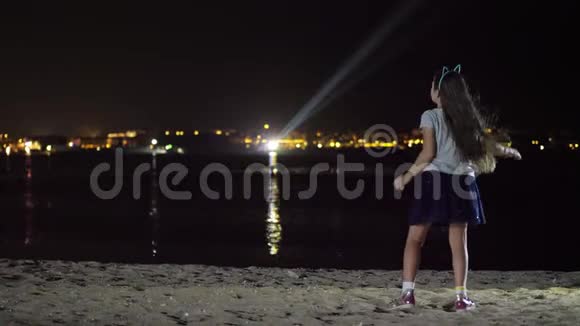 夜晚一个穿着闪亮裙子的少女在跳舞从后面看在发光的城市的灯光下视频的预览图