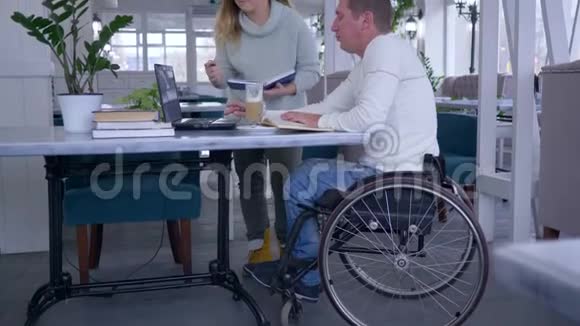 成功的残疾人有创造力的自由职业商人坐在轮椅上和女人讨论用笔记本电脑创业视频的预览图