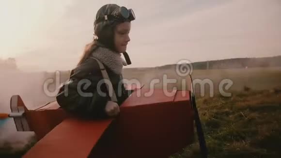 小飞行员女孩跑在有趣的纸板飞机与彩色烟雾后面惊人的秋天日落场慢动作视频的预览图