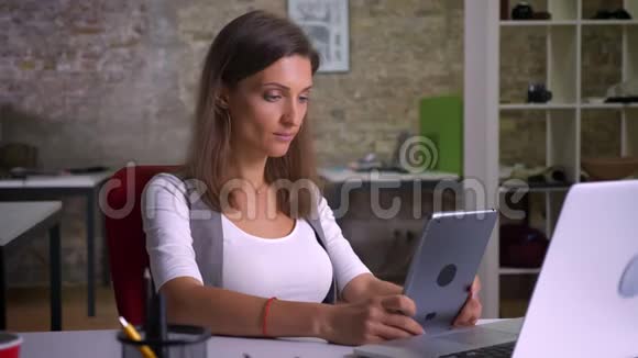 女办公室职员在平板电脑上浏览在室内工作场所微笑视频的预览图