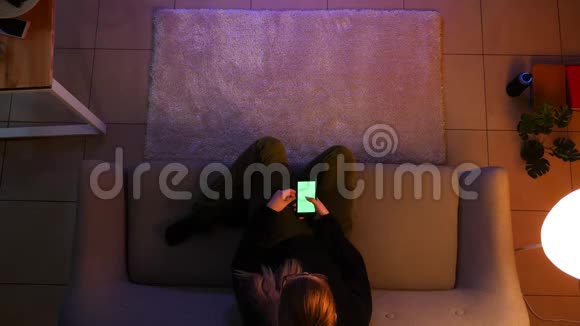 美少女坐在沙发上用绿色屏幕手机看电视的特写镜头视频的预览图