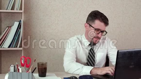 男办公室经理带胡须和眼镜在笔记本电脑后面工作视频的预览图