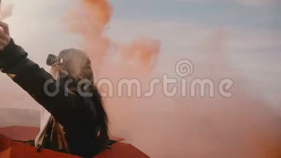 后景小女孩穿着有趣的飞机飞行员服装手里拿着红色的烟雾在日落场上慢动作视频的预览图