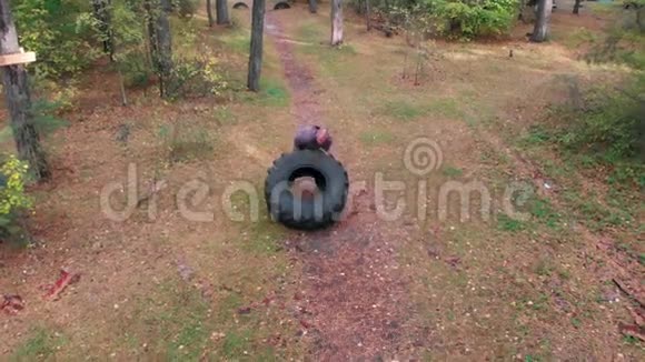 在森林里一个强壮的男性健美运动员把轮胎推到地上视频的预览图