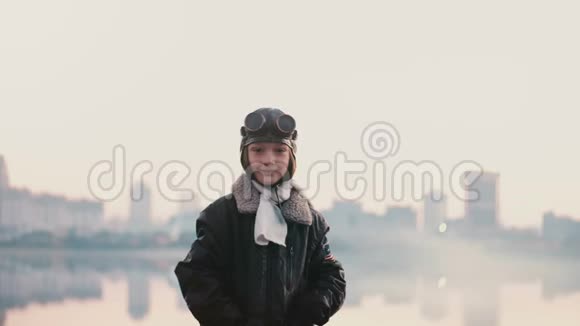 美丽的肖像小女孩穿着旧飞行员服装在日落附近惊人的城市湖泊微笑相机慢动作视频的预览图