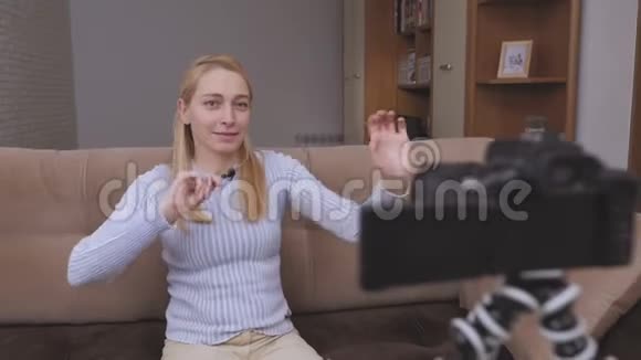 女人视频记录器拍摄vlog坐在沙发上高兴地跳舞而坐在镜头前视频的预览图