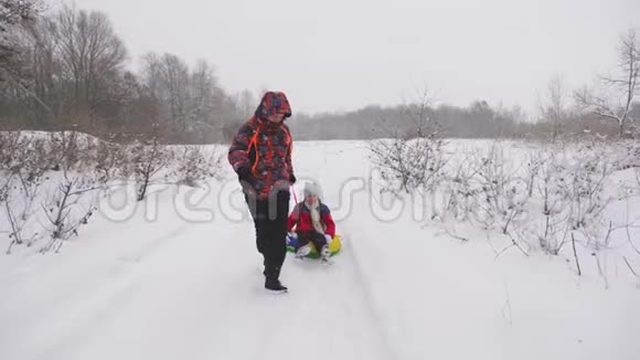 快乐的爸爸骑着一个孩子在白色的雪道上雪橇圣诞节假期成人和儿童的有趣游戏这就是视频的预览图