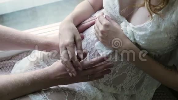 她丈夫旁边穿着白色连衣裙的孕妇正坐在地板上幸福的家庭期待着孩子特写视频的预览图