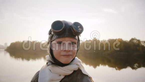 小男孩穿着老式的飞行员服装戴着围巾和眼镜看着相机在湖边做着滑稽的表情视频的预览图