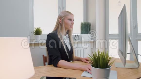 微笑的商务女性竖起大拇指年轻的金发碧眼的年轻女性穿着优雅的西装坐在办公桌前视频的预览图