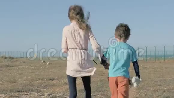 小女孩和小男孩难民走在沙漠里走向用铁丝网围起来的栅栏孩子手里拿着毛绒玩具强迫IMM的概念视频的预览图