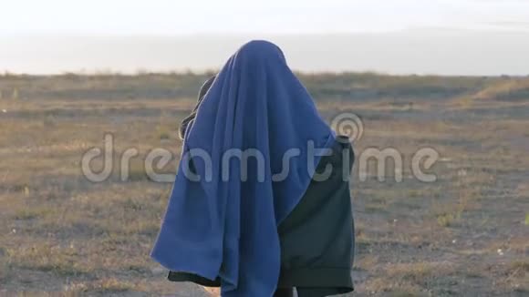 无家可归的小女孩站在田野里用毯子盖住他的头在难民营的领土上玩耍视频的预览图