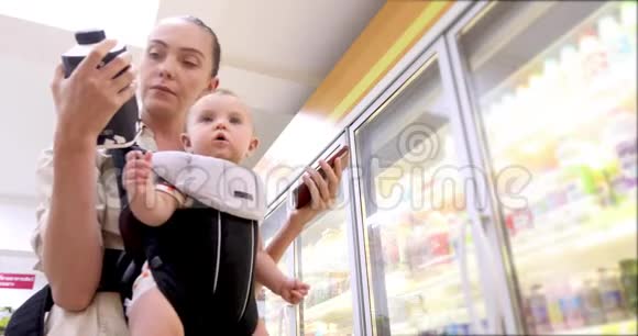 女人在超市和婴儿一起看智能手机视频的预览图