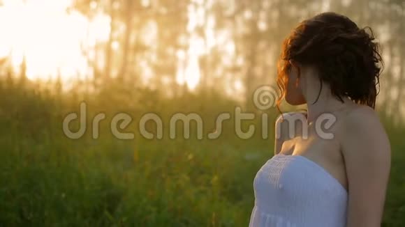 美丽的女孩穿着白色的裙子在阳光明媚的夏天森林里视频的预览图