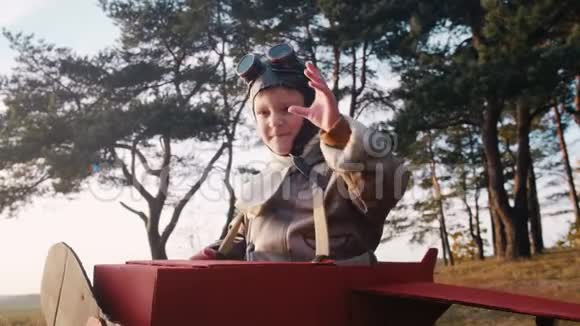 快乐严肃的小飞行员男孩在树下穿着有趣的纸板飞机服装戴着老式航空眼镜慢动作视频的预览图