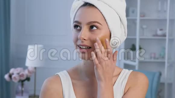 一幅美丽的年轻女子的肖像头上有毛巾用遮瑕膏视频的预览图