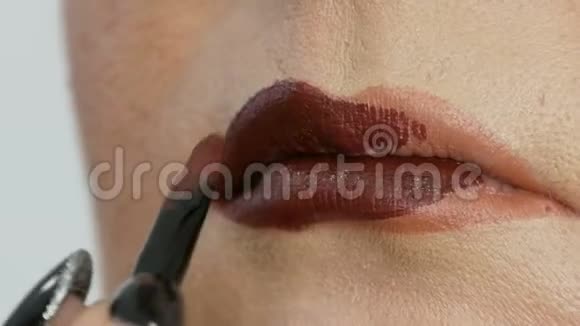 专业主妆师将深红色口红涂在模特薄唇上用特殊的刷子和烟熏妆视频的预览图
