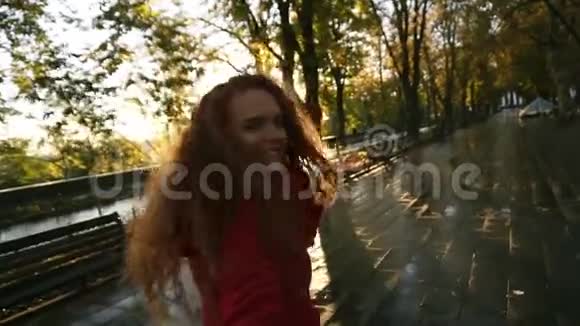 年轻的白种人妇女走在潮湿的小巷旁的一个色彩斑斓的秋天公园里享受着秋天的树叶快乐地转过身视频的预览图