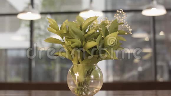 在模糊的背景上玻璃花瓶里的山谷花朵静静地站在木桌上有窗户和灯视频的预览图
