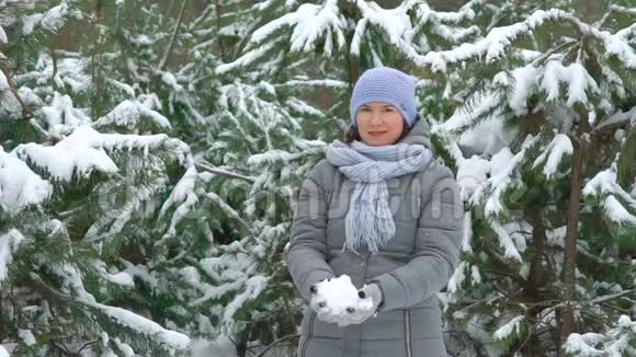 冬天的一天微笑的女人在松林中缓慢地扔雪视频的预览图