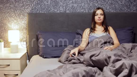 年轻女子躺在床上在家看喜剧表演更换电视遥控器频道视频的预览图