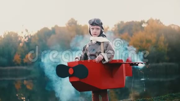 快乐的小飞行员男孩站在日落湖穿着纸板飞机服装彩烟玩飞行员慢动作视频的预览图