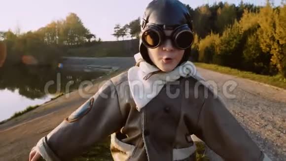 一个快乐的小飞行员男孩戴着老式的飞行员眼镜朝镜头跑去假装是一个飞机慢动作视频的预览图