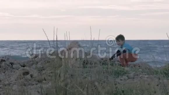 在大海的背景下小流浪汉在刮风的天气里小男孩孤儿在岸上扔石头孤独的概念视频的预览图