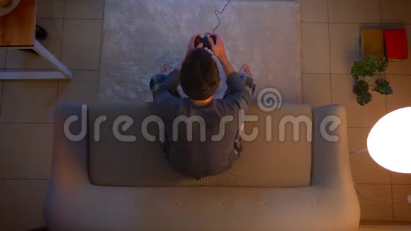 在舒适的家中年轻男性在电视上玩电子游戏使用游戏机坐在沙发上进行特写镜头视频的预览图