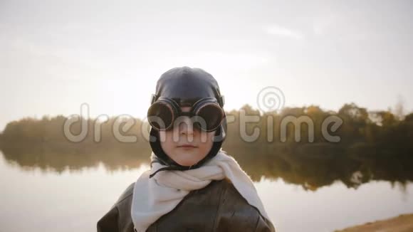 考虑周到的飞行员小男孩看着相机戴着飞行员眼镜竖起大拇指在日落湖慢动作视频的预览图