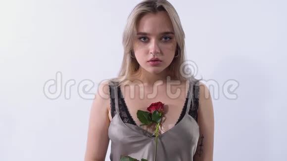 在一个明亮的工作室里一个白色背景上有刺鼻的悲伤女孩的肖像站在玫瑰旁边的漂亮女孩视频的预览图