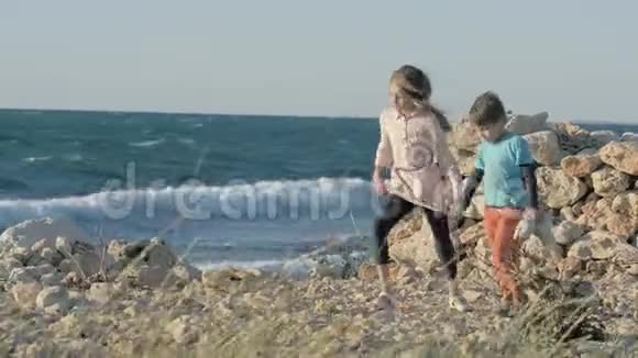 小女孩和男孩在日落时沿着海边散步无家可归的孩子在背景海洋中散步孩子和他的孩子在一起视频的预览图