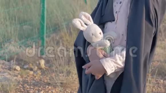 孤儿抱着一个玩具站他的头朝下靠近高栅栏带着铁丝网带着泰迪沮丧的小女孩难民视频的预览图