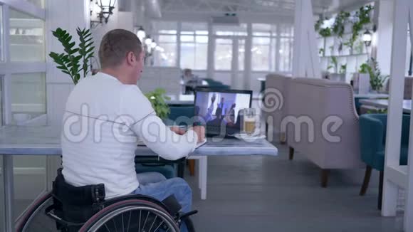 家庭教育坐在轮椅上的残疾老人在笔记本上写笔记同时观看笔记本电脑的在线培训视频的预览图