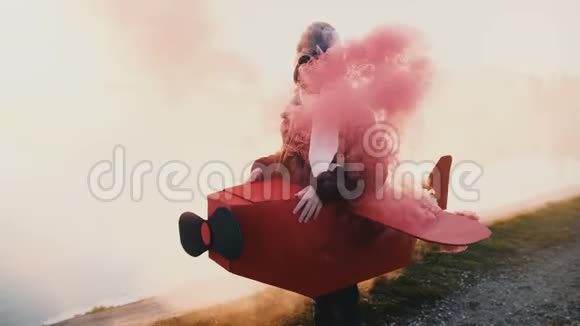 小快乐微笑的女孩穿着有趣的飞机飞行员服装眼镜周围是彩色烟雾外面慢动作视频的预览图
