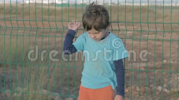由于战争冲突无家可归的年轻难民小男孩站在离城市一个封闭区域的栅栏附近视频的预览图