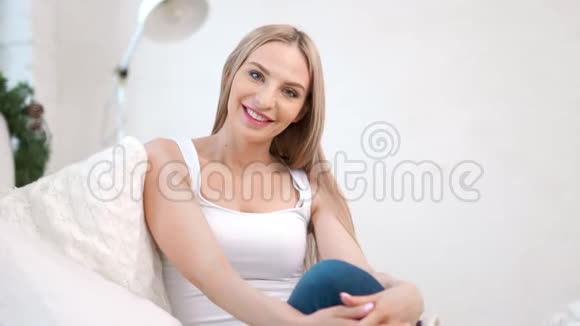 在舒适的白色室内沙发上坐着一位快乐迷人的欧洲女性中镜头画像视频的预览图