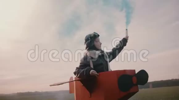 小飞行员女孩跑步穿着有趣的纸板飞机服装与蓝色的烟雾在秋天日落缓慢的运动视频的预览图