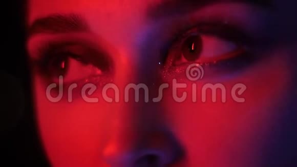 在夜店用红色霓虹灯和bokeh背景的迷人时尚化妆的漂亮女性眼睛特写镜头视频的预览图