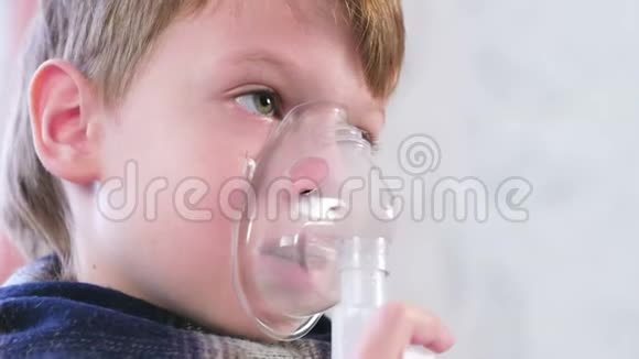生病的金发男孩通过吸入器面罩吸入特写面部侧视图使用雾化器和吸入器进行治疗视频的预览图