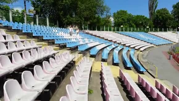 空中视频在体育场新婚夫妇穿着婚纱在白色和蓝色的座位之间行走春天阳光明媚视频的预览图
