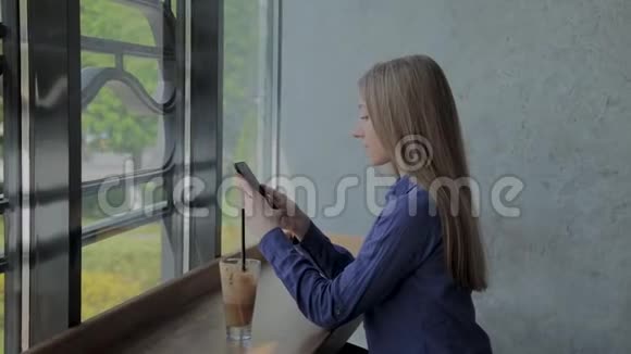 漂亮的女孩坐在窗边桌上放着电话和饮料视频的预览图