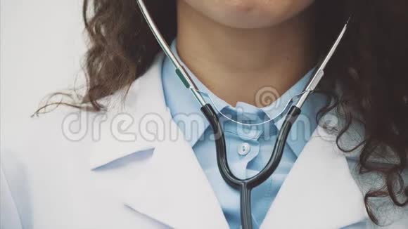 一位年轻的女医生的特写镜头穿着白色长袍站在灰色的背景上拥有视频的预览图
