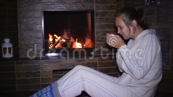 坐在壁炉旁喝茶的漂亮姑娘视频的预览图