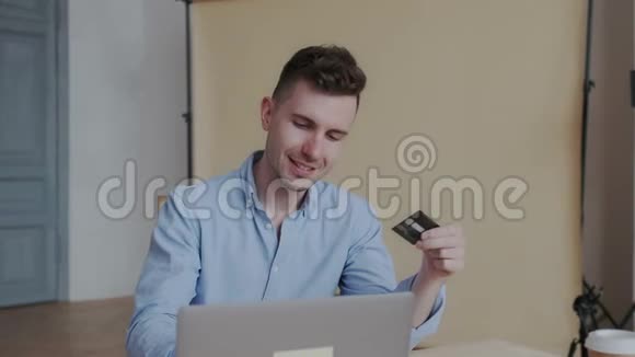 漂亮迷人和快乐的年轻人穿着蓝色衬衫使用笔记本电脑在线购物与信用卡室内快速视频的预览图